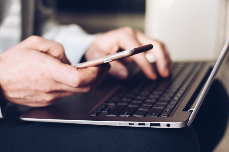 a person holding phone and using a laptop