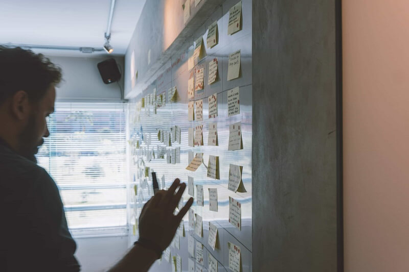 person looking at a board full of passwords on sticky notes