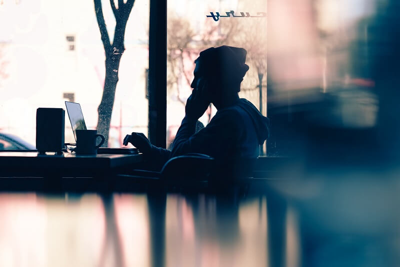 a man scrolling on his laptop and speaking on the phone